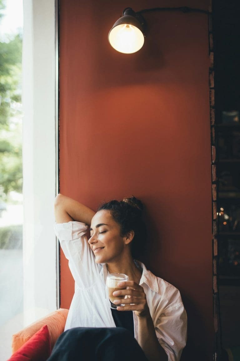 Young woman drinking coffee cappuccino sitting near window.